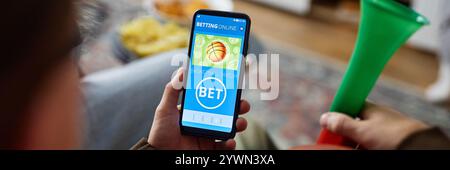 Image d'en-tête de l'homme tenant un smartphone avec l'application de Paris sportifs en ligne sur l'écran tout en regardant un match de basket-ball à la maison, espace de copie Banque D'Images