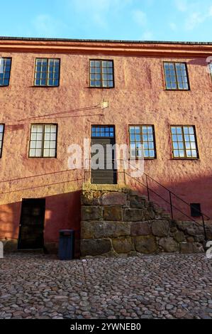 Un bâtiment rose comporte plusieurs fenêtres et une porte noire qui mène à une entrée surélevée. La structure se trouve bien en évidence dans une cour pavée Banque D'Images