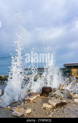 Vagues écrasantes sur une jetée altérée. Des vagues blanches se brisent sur une côte rocheuse. Éclaboussures spectaculaires de mousse de mer contre le béton Banque D'Images