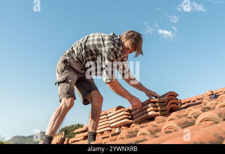 Un couvreur inspectant et réparant un toit par une journée ensoleillée. Travaux d'entretien de la maison. Banque D'Images