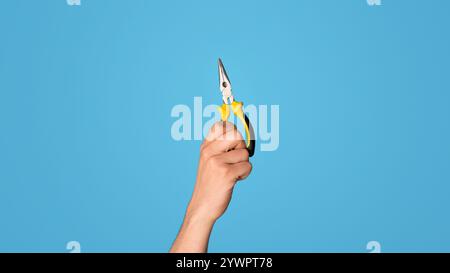 Vue rognée du handyman tenant une pince à bec plat sur fond bleu, gros plan Banque D'Images