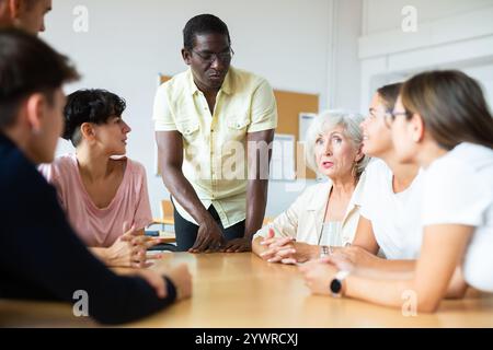 Sympathique tutrice afro-américaine d'anglais donnant des cours de langue à un groupe d'adultes Banque D'Images