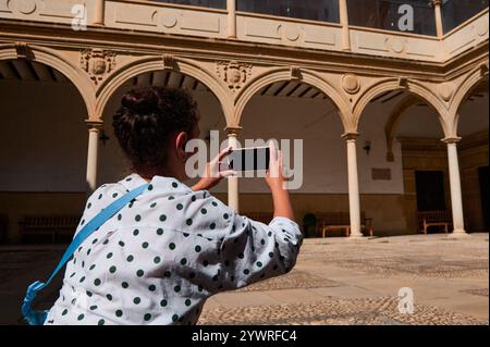 Une touriste saisit la beauté de l'architecture historique dans une cour ensoleillée à l'aide de son smartphone, mettant en évidence les voyages et l'exploration. Banque D'Images