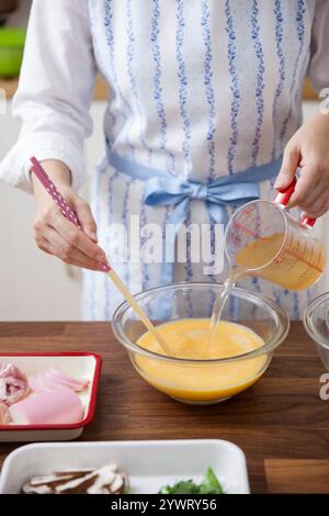 Femme ajoutant du bouillon au mélange d'œufs Banque D'Images