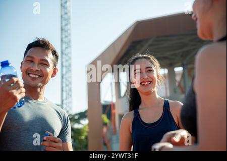 Un groupe d'athlètes asiatiques assistent à une conversation tout en se reposant sur une piste de course après s'être entraînés dans un stade par une journée ensoleillée et lumineuse. personnes et Banque D'Images