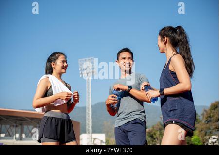 Un groupe d'athlètes asiatiques assistent à une conversation tout en se reposant sur une piste de course après s'être entraînés dans un stade par une journée ensoleillée et lumineuse. personnes et Banque D'Images