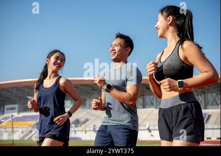 Un groupe de joyeux athlètes asiatiques aiment discuter tout en s'entraînant et en courant dans un stade par une journée ensoleillée et lumineuse. amitié, sport, vie Banque D'Images