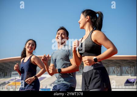 Un groupe de joyeux athlètes asiatiques aiment discuter tout en s'entraînant et en courant dans un stade par une journée ensoleillée et lumineuse. amitié, sport, vie Banque D'Images