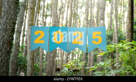 Texte de bonne année 2025 écrit sur papier suspendu avec fond d'arbres. Bonne année concept ou célébration Banque D'Images