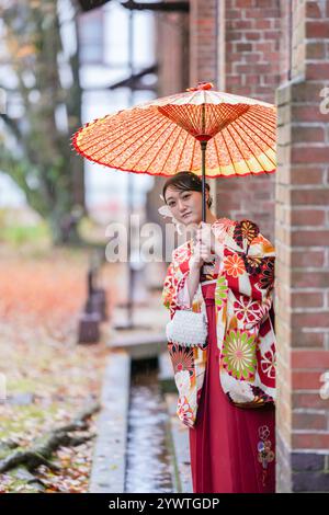 Une femme japonaise dans la vingtaine portant un hakama rouge, un incontournable pour les diplômés d'université japonais, tient un parapluie traditionnel japonais rouge en fr Banque D'Images
