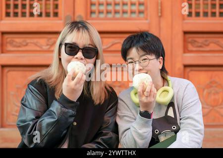 Deux chinoises dans les années 30 mangeant des petits pains cuits à la vapeur devant un bâtiment historique dans le quartier de Jing'an, Shanghai, Chine. Banque D'Images