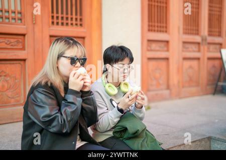 Deux chinoises dans les années 30 mangeant des petits pains cuits à la vapeur devant un bâtiment historique dans le quartier de Jing'an, Shanghai, Chine. Banque D'Images