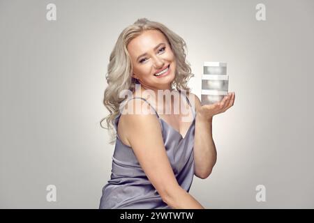 Femme blonde caucasienne de cinquante ans tenant des crèmes pour le visage. Banque D'Images