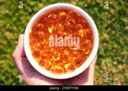 Capsules d'huile de poisson comme suppléments contenant des acides gras oméga-3 qui sont consommés pour des bienfaits pour la santé, dans un bol rond tenu à la main. Banque D'Images
