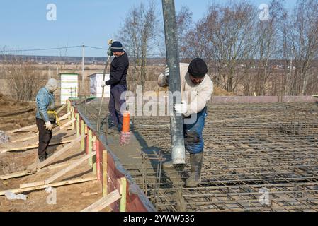 RÉGION DE LENINGRAD, RUSSIE - 28 MARS 2021 : les travailleurs migrants de la construction versent la fondation d'une maison de campagne un jour ensoleillé de mars Banque D'Images