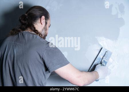 Un plâtre professionnel applique une couche de plâtre décoratif sur le mur. Le concept de rénovation et de réparation. Vue de face Banque D'Images