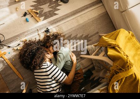 Enfant embrassant sa mère tout en jouant ensemble sur un tapis confortable dans leur salon. La scène représente l'amour, le lien et le confort de la maison. Banque D'Images