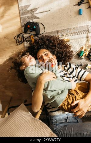 Une mère joyeuse et son jeune fils partagent des moments joyeux en jouant sur le sol du salon, entourés de jouets mettant en valeur le lien familial et le bonheur. Banque D'Images