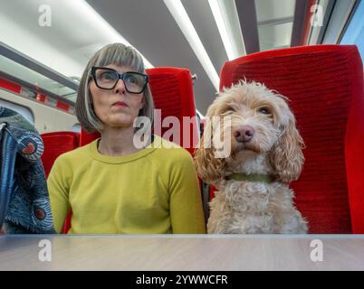 Femelle caucasienne mature assise sur un train vide avec un chien Cockapoo de couleur crème. ROYAUME-UNI Banque D'Images