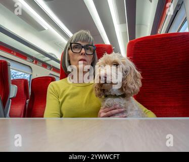 Femelle caucasienne mature assise sur un train vide avec un chien Cockapoo de couleur crème. ROYAUME-UNI Banque D'Images