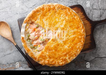 Tarte au saumon maison avec carottes, maïs, oignon et petits pois et dans une croûte de tarte au beurre en gros plan sur le plat de cuisson sur la table. Vue horizontale du dessus Banque D'Images