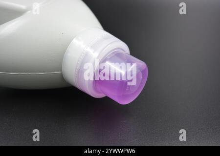 Une grande bouteille grise pour laver les vêtements, linge de lit, tissus. Une bouteille en plastique remplie d'un liquide visqueux violet avec un bouchon transparent. Banque D'Images