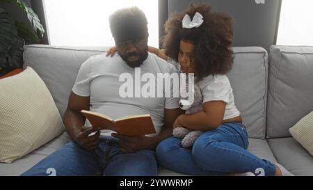 Père lisant livre à sa fille dans un salon confortable montrant l'amour familial chaleureux et le lien dans un cadre intérieur sur un canapé confortable. Banque D'Images