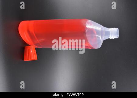Une grande bouteille transparente pour laver les vêtements, le linge de lit, les tissus et les salles de nettoyage. Une bouteille en plastique remplie d'un liquide rouge avec un bouchon rouge vif Banque D'Images