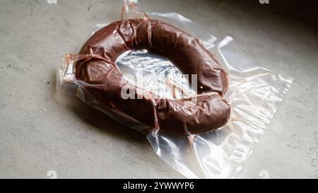 Saucisse scellée sous vide sur une surface en béton gris présentant de la viande fraîche et emballée pour le stockage ou la conservation des aliments dans un cadre de cuisine Banque D'Images