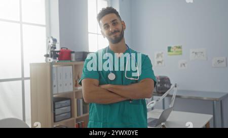 Un beau jeune homme hispanique en gommage se tient confiant avec les bras croisés dans un lieu de travail de clinique vétérinaire avec du matériel médical et du drawin animal Banque D'Images