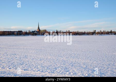Un paysage hivernal serein capturé à Mora, Dalarna, Suède. La scène met en valeur une vaste étendue enneigée avec une tour d'église visible au loin agai Banque D'Images