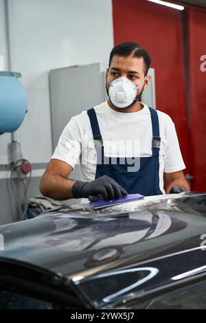 Focused Mechanic prépare une surface de voiture tout en portant des gants et un masque de protection pour les détails. Banque D'Images