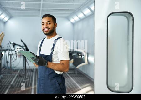 Beau jeune mécanicien tient un presse-papiers, mettant en valeur le professionnalisme dans un atelier élégant. Banque D'Images