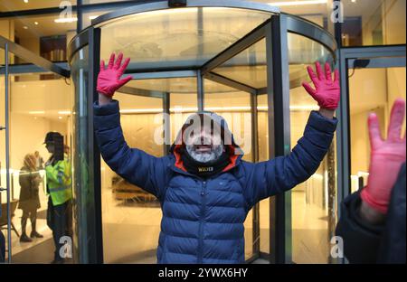 Bimingham, Angleterre, Royaume-Uni. 12 décembre 2024. Un activiste proteste à l'extérieur tenant ses mains rouges en l'air et scandant alors que les policiers s'assurent que la réception reste claire pendant la manifestation. Les militants pro-palestiniens ciblent les bureaux d'assurance d'Allianz dans leur Colmore Building, Birmingham, occupant la zone de réception et manifestant à l'extérieur. Ils ciblent Allianz parce qu’ils assurent et investissent dans la société israélienne d’armement Elbit Systems et sont déterminés à maintenir la pression de l’action directe afin que cela devienne un inconvénient majeur de travailler avec eux. Ils exigent que la société abandonne Elbit Sys Banque D'Images