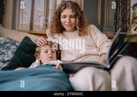 Séance de lecture cosy de Noël entre mère et enfant au coin de la cheminée un soir d'hiver Banque D'Images