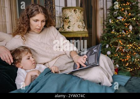 Cozy session de lecture du réveillon de Noël près de la cheminée avec l'enfant et la mère pendant la saison des fêtes Banque D'Images