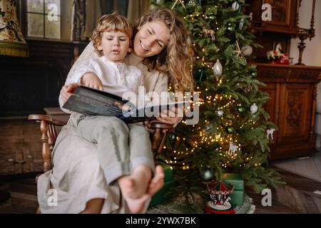 Moments de vacances confortables avec la lecture d'enfant par le sapin de Noël dans le cadre chaleureux du salon Banque D'Images