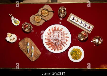 Une table à manger vibrante avec un éventail de plats gastronomiques. Au centre, une assiette magnifiquement agencée de jambon séché est entourée de verres élégants Banque D'Images