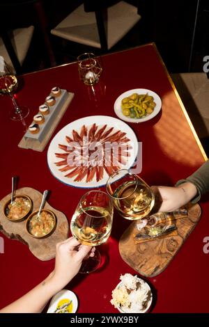 Deux mains claquent leurs verres de vin blanc lors d'un dîner romantique. Banque D'Images