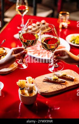 Deux mains claquent leurs verres de vin blanc lors d'un dîner romantique. Banque D'Images