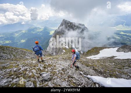 Alpiniste avec casque sur un sentier de randonnée étroit, ascension à l'Ackerlspitze, nuages se déplaçant autour des montagnes, Wilder Kaiser, montagnes Kaiser, Tyr Banque D'Images