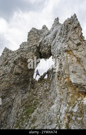 Alpiniste avec casque debout dans une arche rocheuse, ascension vers le Maukspitze, nuages se déplaçant autour des montagnes, Ackerlpitze en arrière-plan, Wilder K Banque D'Images