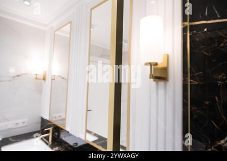 Une salle de bains avec des carreaux de métro verticaux en marbre et empilés, un meuble-lavabo en chêne blanc, des miroirs carrés encadrés de noir et des robinets, et un comptoir en marbre. Banque D'Images
