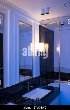Une salle de bains avec des carreaux de métro verticaux en marbre et empilés, un meuble-lavabo en chêne blanc, des miroirs carrés encadrés de noir et des robinets, et un comptoir en marbre. Banque D'Images