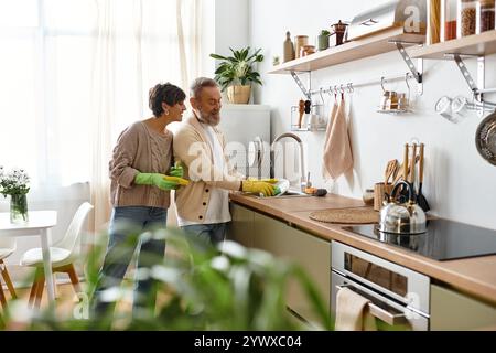 Un couple mûr apprécie la compagnie de l'autre tout en lavant la vaisselle dans une cuisine ensoleillée. Banque D'Images