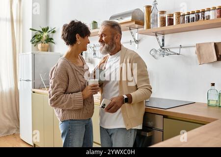 Un couple mûr aime la compagnie de l'autre tout en discutant et en souriant dans leur cuisine accueillante. Banque D'Images