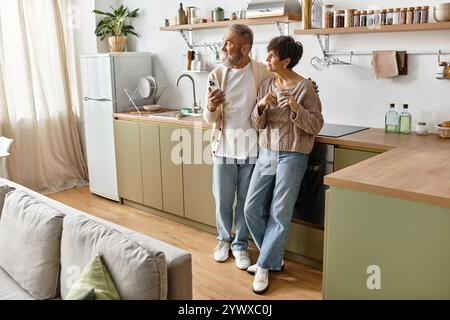 Un couple mûr apprécie la compagnie de l'autre tout en sirotant des boissons dans un cadre de cuisine chaleureux. Banque D'Images