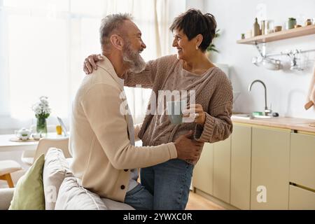 Un couple mûr apprécie la compagnie les uns des autres dans une cuisine confortable, partageant rire et chaleur. Banque D'Images