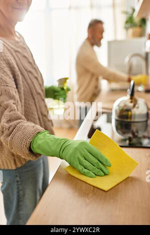 Un couple mûr partage un moment joyeux alors qu'ils nettoient leur maison, mettant en valeur le travail d'équipe et l'amour. Banque D'Images