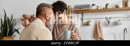 Un couple mûr partage un moment joyeux, souriant et s’embrassant dans une cuisine chaleureuse. Banque D'Images